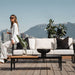 Front View of the Francis Outdoor Rectangular Coffee Table On a Patio With Woman Sitting On a Couch Arm in the Background