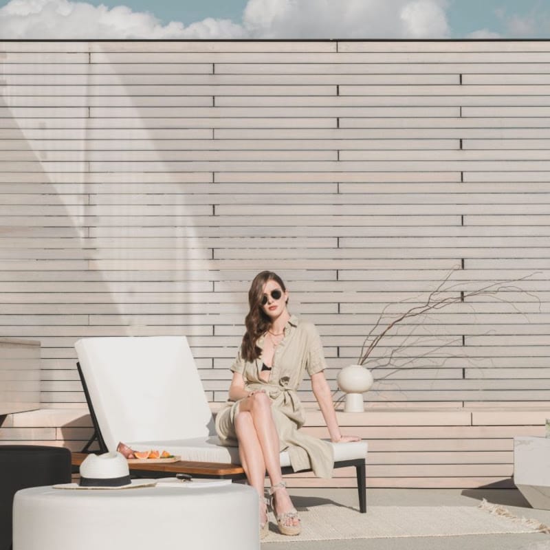 Woman Sitting At The Edge of a Francis Outdoor Lounger In Palisades Color With Black Base