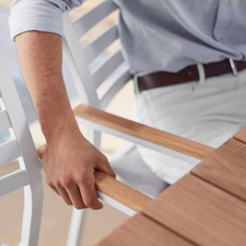 Close Up View Of Man Holding The Arm Of a Linnea Outdoor Dining Chair In Encino Fabric With White Frame