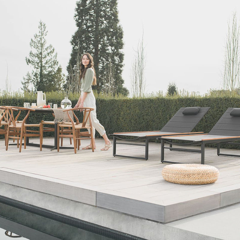 Woman Standing By a Table Next to Two Linnea Outdoor Loungers in Black