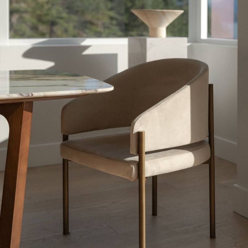 Sun Shining on a Solana Dining Chair in Latte Fabric and Antique Brushed Brass Base at a Dining Table