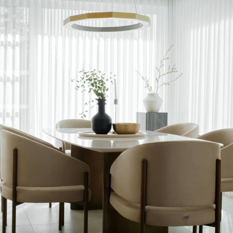 Several Solana Dining Chairs in Latte Fabric and Antique Brushed Brass Base at a Dining Table Next to a Window With Curtains