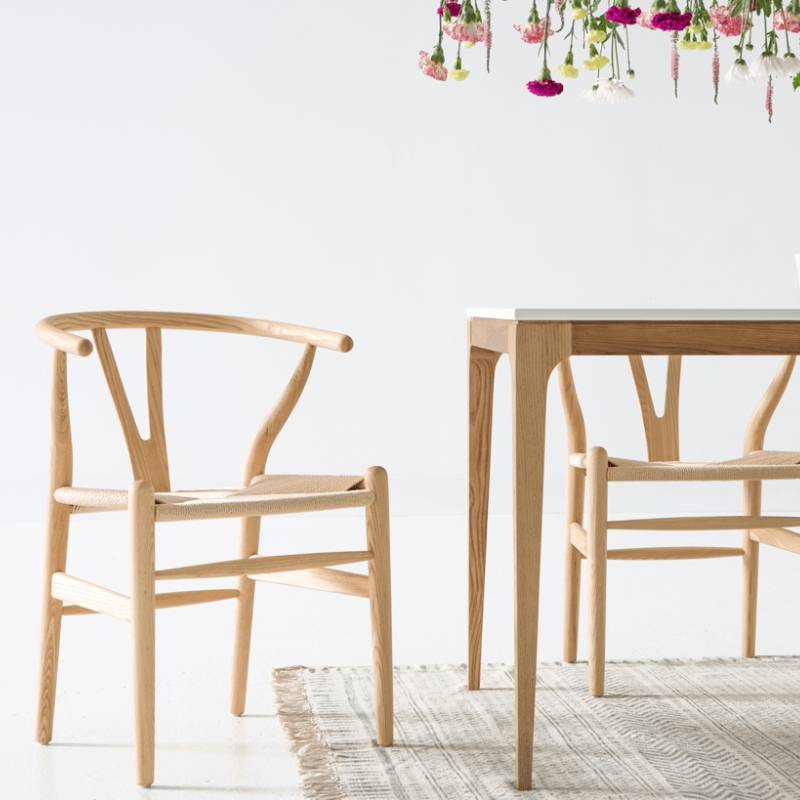 Two Wishbone Chairs in Natural Seat Cord and Natural Wood Finish at a Dining Table With a Bright White Background