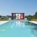 Yolo Outdoor TV Wall Mounted at The Edge of a Pool With House in The Background