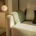 A Liza Side Tables (Black Label) in White Travertine in the Background With a Lamp on Top of It