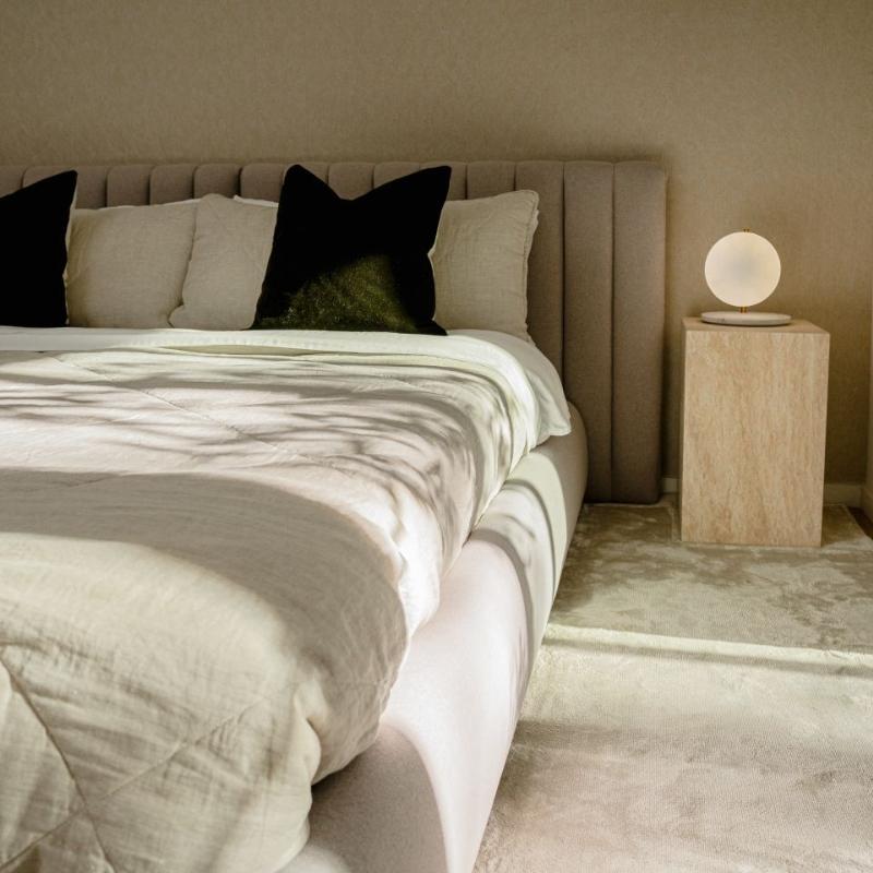 A Liza Side Tables (Black Label) in White Travertine on The Right Side of a Bed