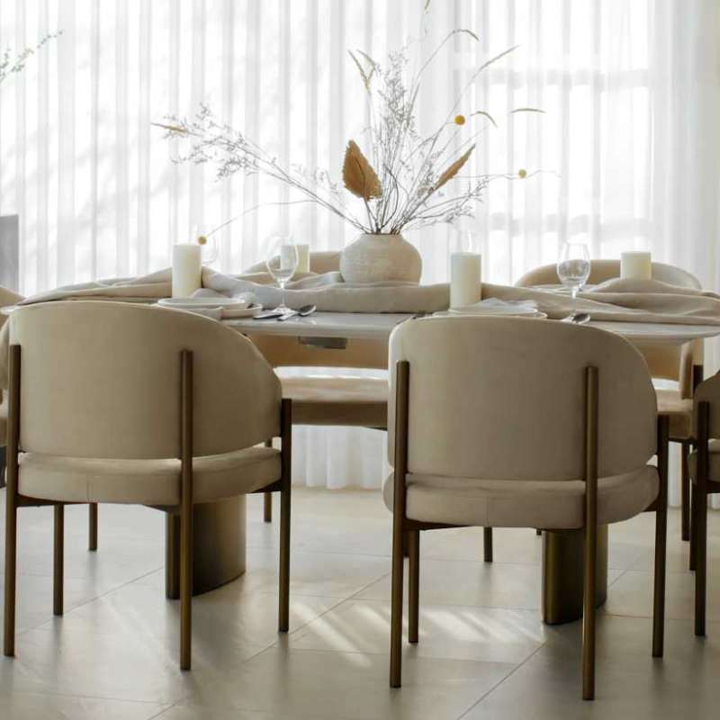 Angled Top View of The Solana Dining Table With a White Calacatta Ceramic Surface and Antique Brushed Brass Base in a Dining Area Next to a Window